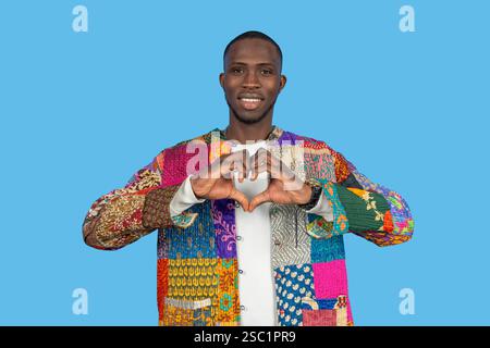 Stylish man forming heart shape with hands, expressing love and positivity on vibrant blue backdrop Stock Photo