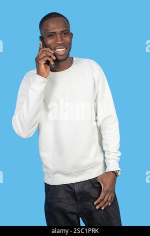 Young adult man making a phone call and smiling with blue background Stock Photo