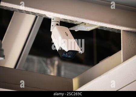 A security camera mounted on a metal beam under the ceiling of a large arena. Stock Photo
