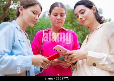 Three Young Women Using Smartphones Outdoors Stock Photo