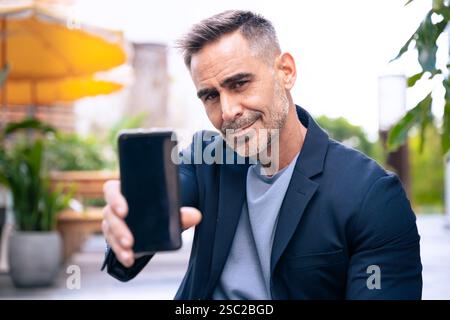 Confident Man Holding Smartphone Outdoors with a Subtle Smile Stock Photo