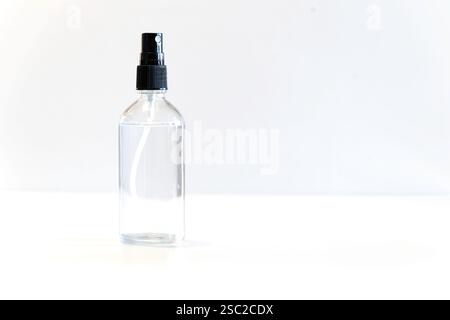 Small glass bottle with spray cap on bright background. The bottle is filled with a transparent liquid Stock Photo