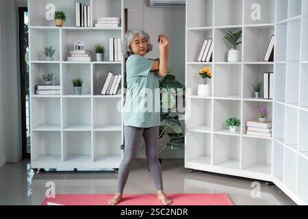 Senior woman performing stretching exercises at home, focusing on wellness and mobility. Stock Photo