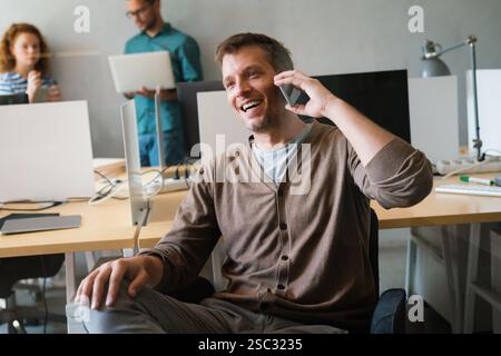 Happy startup business man, programmer, freelancer discussing on mobile phone while looking away. Stock Photo