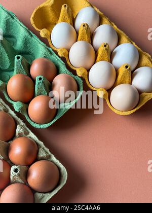 White and brown chicken eggs in multicolored paper cartons on a peachy background Stock Photo