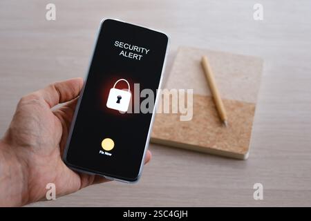 Hand holding smartphone displaying security alert with lock icon Stock Photo