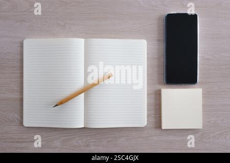 Open notebook with pen next to smartphone and sticky notes on wooden desk Stock Photo