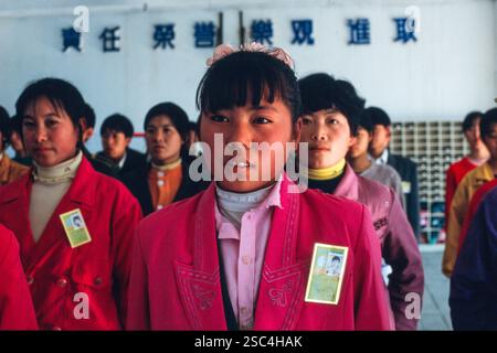 A group of women shoe factory workers stand indoors with identification cards in China. Stock Photo