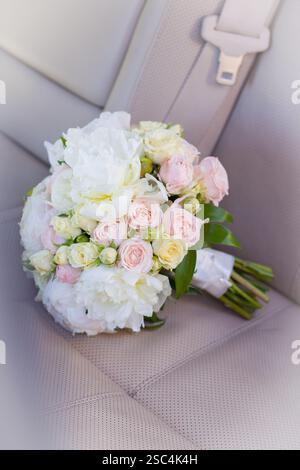 Bridal bouquet of white peonies and soft pink roses in delicate pastel shades on a beige leather car seat Stock Photo