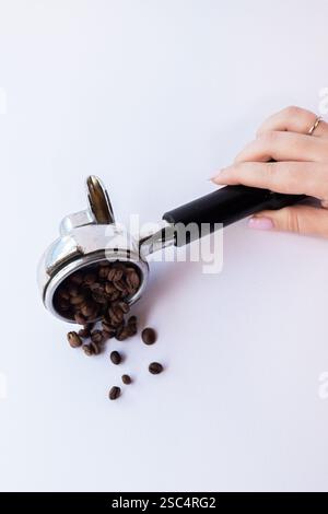 Espresso machine portafilter filled with whole roasted coffee beans, lying on a bright white background. Minimalist studio shot. Stock Photo