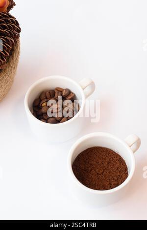 Two small white cups containing whole roasted coffee beans and ground coffee, side by side on a clean white background. Top view, contrast concept. Stock Photo