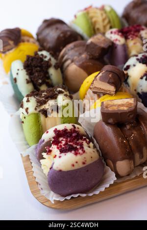 Assortment of colourful macarons and chocolate-glazed truffles served on a wooden board. Selection of various sweet desserts decorated with chocolate. Stock Photo