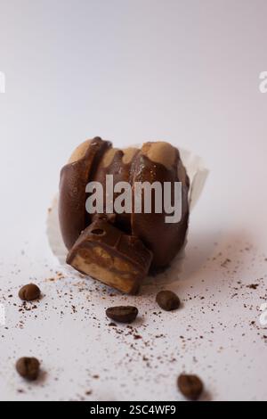 Delicious chocolate macaron (macaroon) with a half piece of chocolate candy, coffee beans and grounds scattered around. Sweet dessert. Stock Photo
