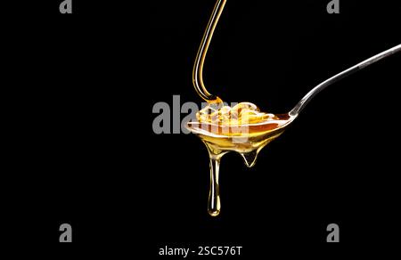 A spoonful of delicious honey spilling on a black background Stock Photo