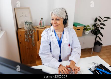 Senior doctor in white coat working on desktop PC at hospital office desk Stock Photo