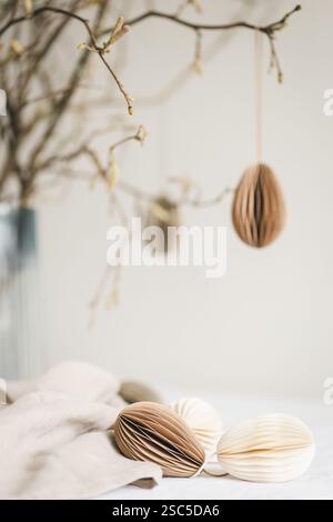 Paper Easter eggs hanging on branches under table with decorations on it. Stock Photo