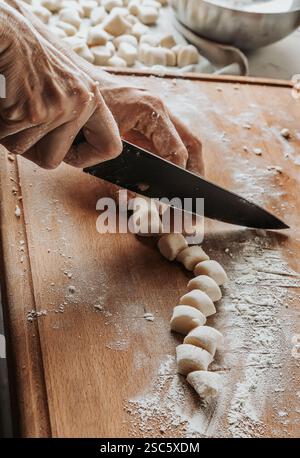 Homemade pasta preparation in Tuscany. The image shows the hands of a woman rolling, shaping and cutting fresh pasta dough, pappardelle & gnocchi. Stock Photo