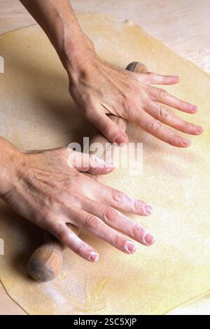 Homemade pasta preparation in Tuscany. The image shows the hands of a woman rolling, shaping and cutting fresh pasta dough, pappardelle & gnocchi. Stock Photo