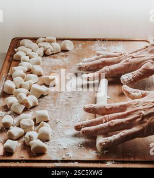 Homemade pasta preparation in Tuscany. The image shows the hands of a woman rolling, shaping and cutting fresh pasta dough, pappardelle & gnocchi. Stock Photo