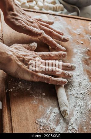 Homemade pasta preparation in Tuscany. The image shows the hands of a woman rolling, shaping and cutting fresh pasta dough, pappardelle & gnocchi. Stock Photo