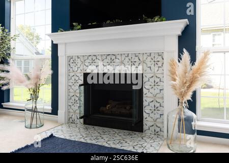 A fireplace detail with a white mantel surrounding white pattern tile on blue walls with bright windows surrounding. Stock Photo