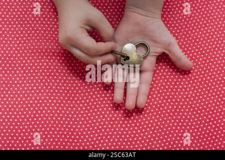 Hand holding a heart shaped lock and key on a red background Stock Photo
