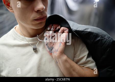 Cropped shot of male artists hand stained with paint holding hanger with jacket over shoulder while coloring designer clothing in workshop Stock Photo