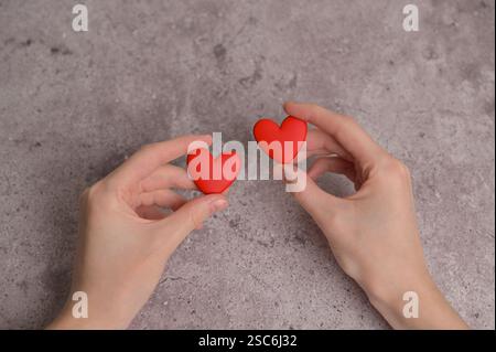Woman holding couple of red earrings heart shape in hands. Gray concrete background. Blood donor donation Stock Photo
