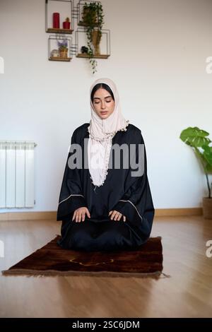 Muslim woman praying on rug at home Stock Photo