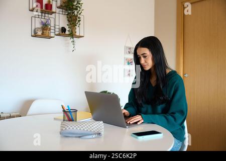 Focused young woman working from home on laptop at table Stock Photo