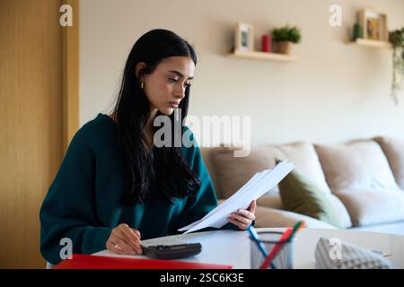 Young woman managing home finances and calculating expenses at home Stock Photo