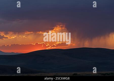 sun setting over Montana hills behind rain and rain clouds Stock Photo