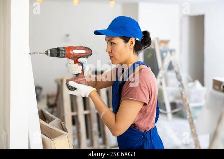 Woman builder using drill to bore hole in wall Stock Photo