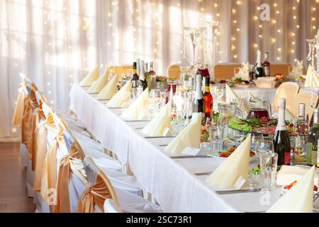Decorated festive table in a banquet hall decorated for the holiday with bottles of wine, glasses, plates and other dishes Stock Photo