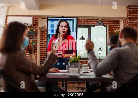 Coworkers using digital screen to discuss startup project with remote female client during videoconference. Diverse team collaborates with woman analyst on virtual call, discussing in meeting room. Stock Photo