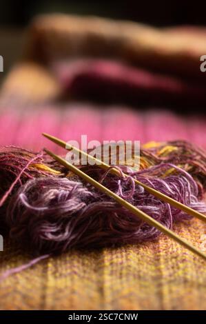 Knitting needles with pink purple, and gold fingering yarn and finished scarf out of focus Stock Photo