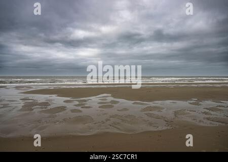 A cloudy sky over a deserted beach with wet sand and gentle waves. Stock Photo