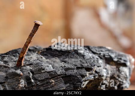 Bent and rusty nail on the left side stuck in a piece of burnt wood Stock Photo