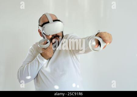 Adult man in VR headset aiming with controllers on a white background Stock Photo