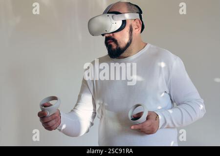 Serious adult man in white with VR headset holding the controllers on white background Stock Photo