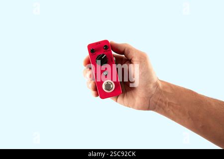 Male hand holding a pink guitar effects pedal isolated on cyan background cutout Stock Photo