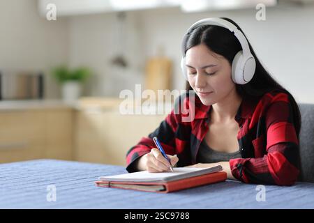 Asian student listening lesson and taking notes in the kitchen at home Stock Photo