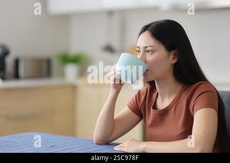 Asian woman drinking tea sitting in the kitchen at home Stock Photo