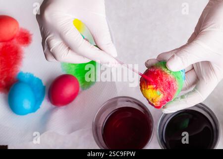Preparing for Easter - coloring eggs in home kitchen female hands in rubber gloves use spoon take boiled egg out of glass with diluted blue dye next o Stock Photo