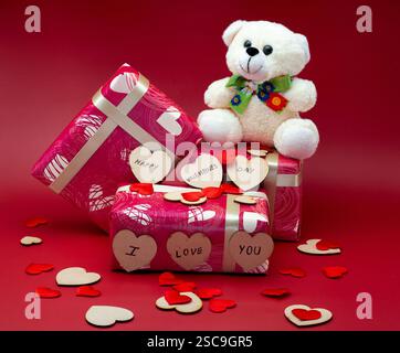 Wrapped gift boxes with a teddy isolated on a red background with small hearts Stock Photo