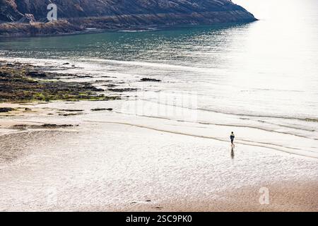Person walking by the waters edge on a sandy beach with rolling waves Stock Photo