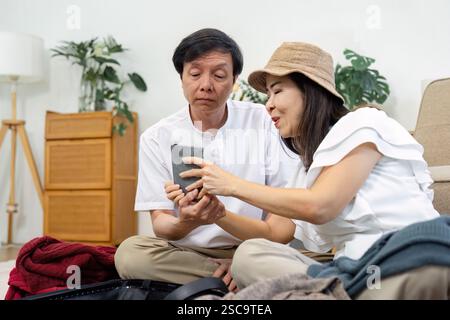 Engaged senior couple reviewing travel plans on a smartphone at home, showcasing their excitement for upcoming adventures. Stock Photo