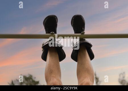 Close-up of men's legs in gravity boots on a horizontal bar. View from below, focus on the legs, exercise for the back. Stock Photo