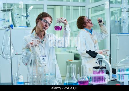 Two Walking Dead Lab Technicians in Bloody Coats Working with Reagents Stock Photo