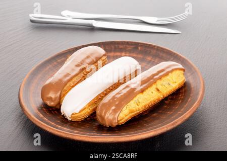 Three eclairs with cream filling on a clay plate on a slate stone. Stock Photo